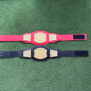 May include: Two championship belts, one red and one black, with gold accents and a blank space for a name or logo.