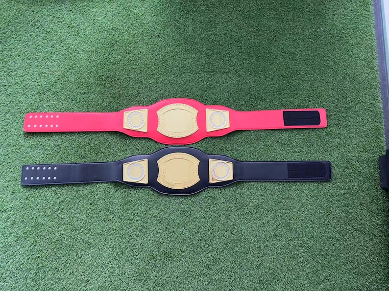 May include: Two championship belts, one red and one black, with gold accents and a blank space for a name or logo.