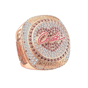 Puede incluir: Anillo de oro rosa con una cara redonda, incrustado con piedras preciosas claras y rosas. La palabra "Crush" está en escritura rosa en el centro. El anillo está inscrito con "Double Crown Champions" y otro texto.