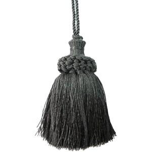 May include: A dark grey decorative tassel featuring a braided cord top, a woven knot neck, and a full skirt of fine, hanging threads. The entire structure is composed of matching dark grey textile fibres, creating a uniform and monochromatic appearance.