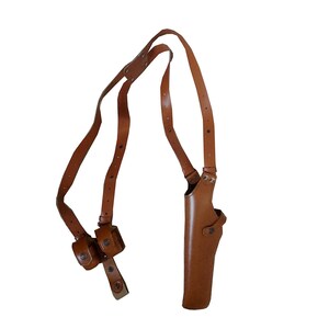 May include: A brown leather shoulder holster with a single gun compartment and two small pouches. The holster has adjustable straps and a buckle closure. The leather appears to be well-worn.