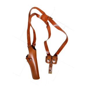 May include: A brown leather shoulder holster with a vertical gun pocket and two small pouches. The holster has adjustable straps and is designed to be worn across the chest and back. The leather has a smooth finish.