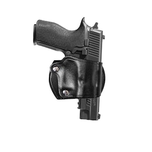 May include: Black handgun in a black leather holster. The handgun is partially visible, with the grip and slide clearly shown. The holster is designed to securely hold the firearm, with visible stitching and metal rivets. The background is plain white.