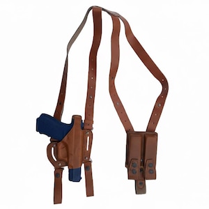 May include: A brown leather shoulder holster with a blue handgun. The holster has a vertical design with straps that go over the shoulders. There is a pouch for extra magazines. The background is white.