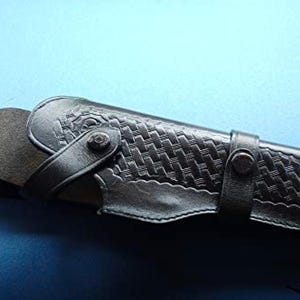 May include: A black leather holster with a woven pattern and a snap closure. The holster has a belt loop and a strap to secure the weapon.