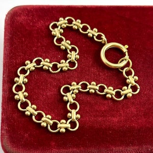 May include: A gold chain bracelet with a delicate design featuring small round beads and interlocking links. The bracelet has a simple clasp.