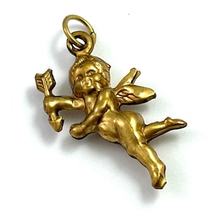 May include: Gold-toned metal charm of a winged cupid holding an arrow. The charm has a loop at the top for attaching to a necklace or bracelet.