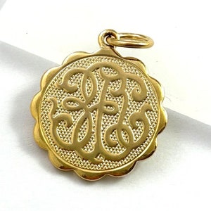 May include: A gold-colored pendant with a scalloped edge and a monogram design in the center.