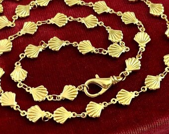Può includere: Una collana a catena d'oro con un design a conchiglia. La catena è composta da piccole conchiglie collegate.