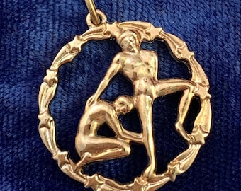 May include: Gold-toned pendant featuring a circular design with two figures, one standing and one kneeling, surrounded by a border of stars.