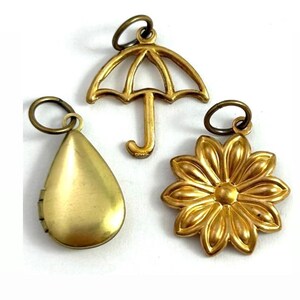May include: Three gold-toned metal charms: a teardrop-shaped locket, a flower with a raised center, and an umbrella with a simple design.