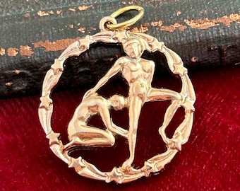 May include: Gold-toned pendant featuring a circular design with two figures in a stylized embrace. The figures are surrounded by a border of stars.