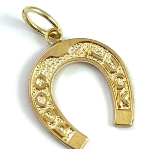 May include: A gold-colored horseshoe pendant with the word "LUCK" inscribed. The pendant has a textured surface and a small loop for a chain. The horseshoe shape is a classic symbol of good fortune.