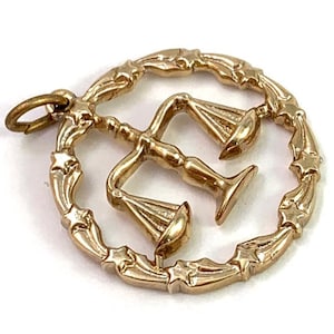 May include: Gold-toned pendant charm featuring a stylized depiction of a scale of justice within a circle of stars.
