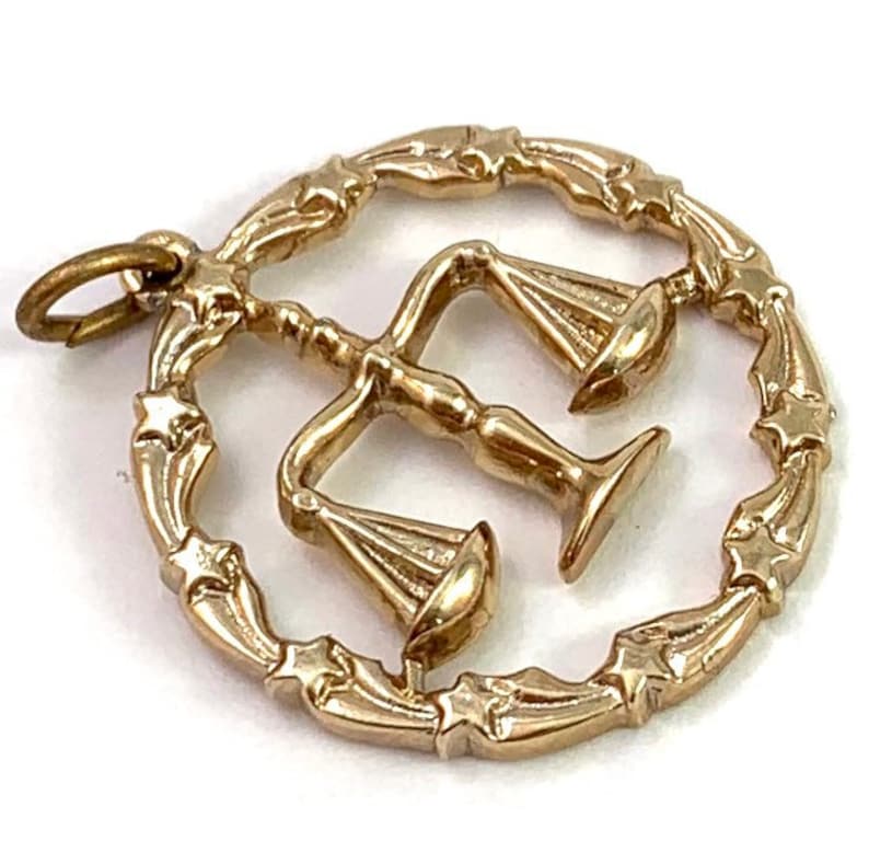 May include: Gold-toned pendant charm featuring a stylized depiction of a scale of justice within a circle of stars.