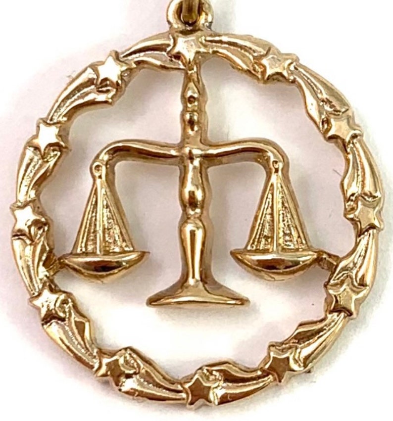 May include: Gold-tone zodiac pendant charm featuring the Libra symbol, a set of scales, surrounded by a circle of stars.