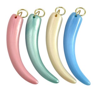 May include: Four curved, horn-shaped pendants in pastel colors: pink, seafoam green, cream, and light blue. Each pendant has a gold-colored ring at the top for hanging. The pendants are smooth and glossy, with a slight pearlescent sheen.