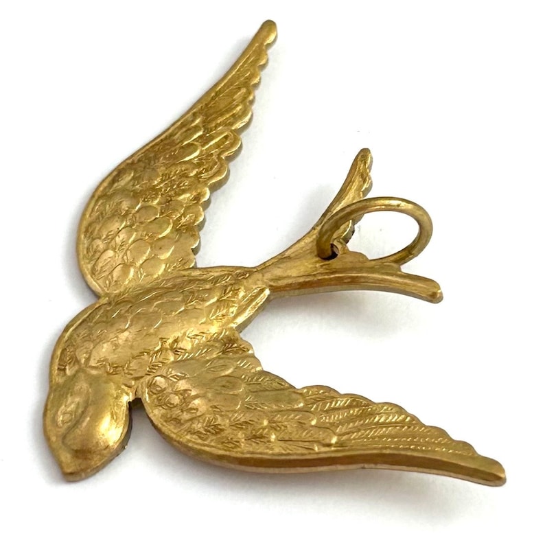 May include: Gold-toned metal bird charm with detailed wings and a ring for attaching to a necklace or bracelet.