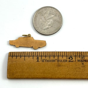 Puede incluir: Un amuleto de coche de color dorado en forma de coche antiguo, que mide aproximadamente 2,5 cm de largo. El amuleto se muestra junto a una moneda de 25 centavos de d&oacute;lar estadounidense para comparar el tama&ntilde;o.