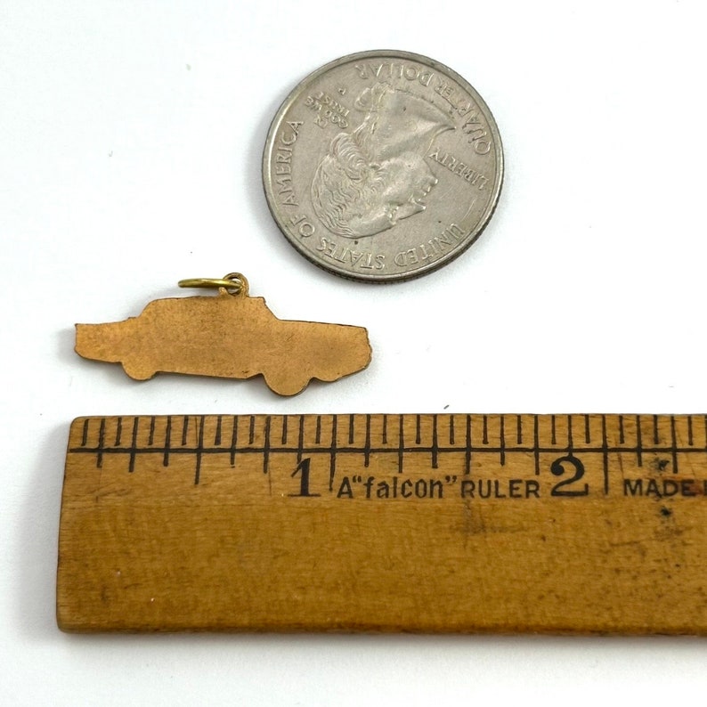 Puede incluir: Un amuleto de coche de color dorado en forma de coche antiguo, que mide aproximadamente 2,5 cm de largo. El amuleto se muestra junto a una moneda de 25 centavos de d&oacute;lar estadounidense para comparar el tama&ntilde;o.