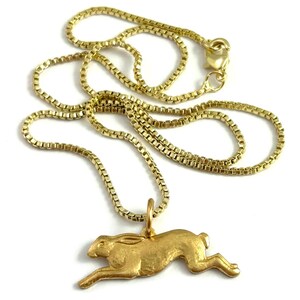 May include: A gold chain necklace with a gold rabbit pendant. The rabbit is in a running pose.