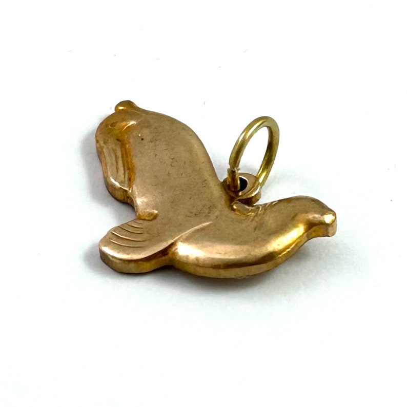 May include: A gold-toned metal dove charm with a ring for attaching to a necklace or bracelet.
