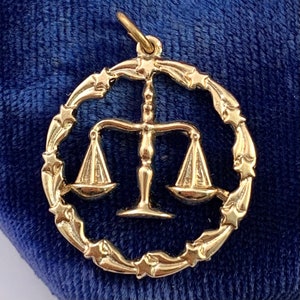 May include: Gold-tone charm featuring a Libra zodiac symbol with a scale design surrounded by a circle of stars.
