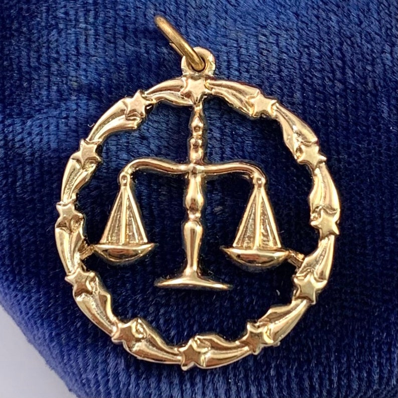 May include: Gold-tone charm featuring a Libra zodiac symbol with a scale design surrounded by a circle of stars.