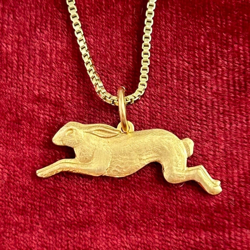 May include: A gold-toned necklace with a pendant shaped like a running hare. The pendant is detailed and has a textured finish.