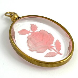 May include: Oval shaped glass pendant with a gold tone metal frame. The glass features a pink rose carved into the glass.