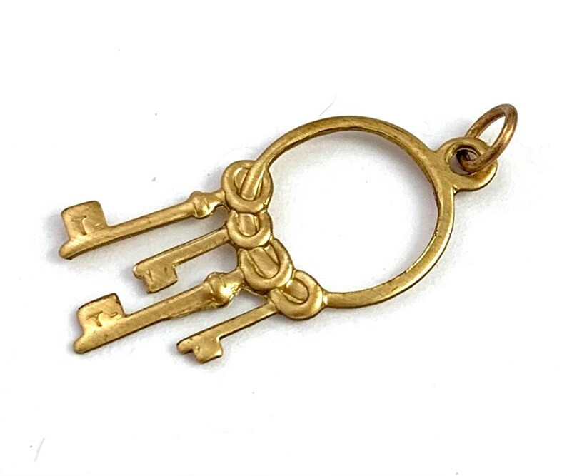 Op de afbeelding: Gouden hanger met een cirkel waaraan vier sleutels hangen. De sleutels zijn met een decoratief knoopje aan de cirkel bevestigd.