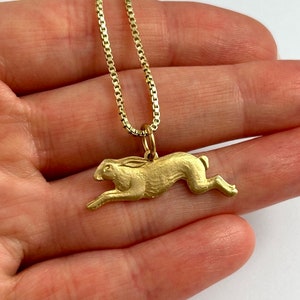 May include: A gold chain necklace with a gold rabbit pendant. The rabbit is depicted in a running pose.