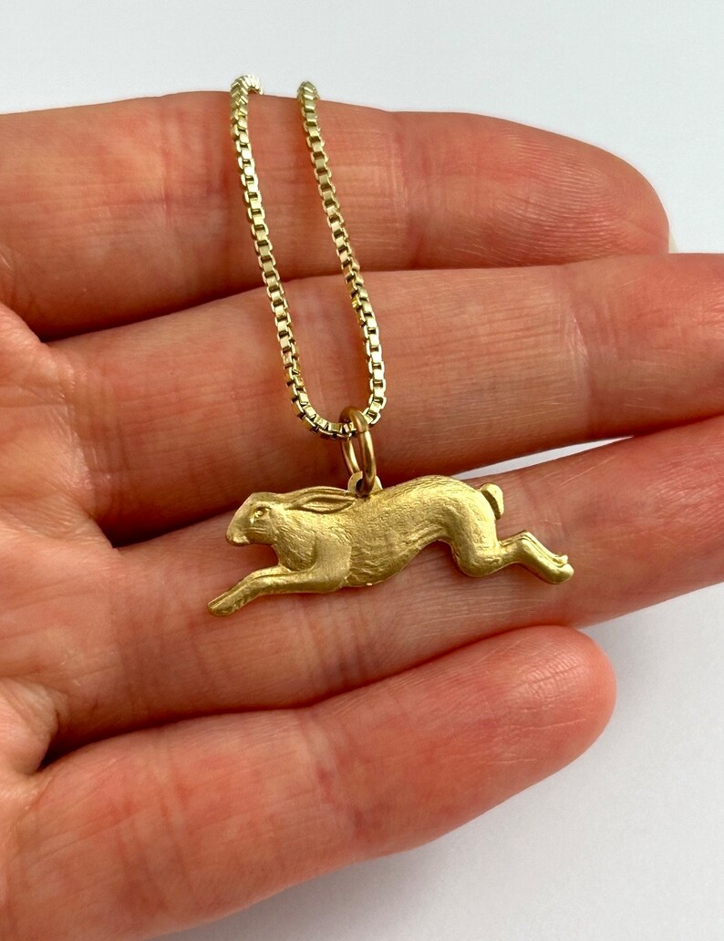 May include: A gold chain necklace with a gold rabbit pendant. The rabbit is depicted in a running pose.