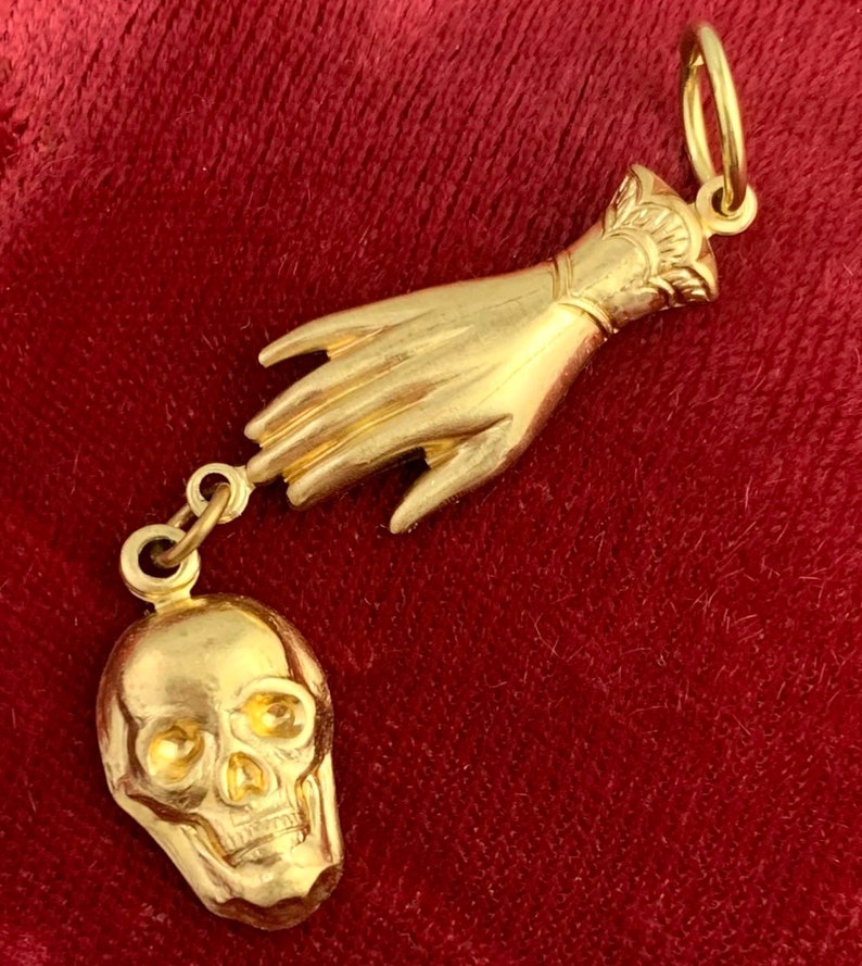 Op de afbeelding: Een gouden ketting met een bedel in de vorm van een hand die naar een schedel reikt.