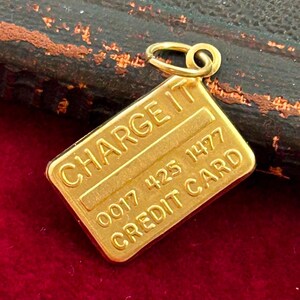 May include: Gold-coloured charm shaped like a credit card with the words "CHARGE IT" and "CREDIT CARD" and the number "0017 425 1477" on it.