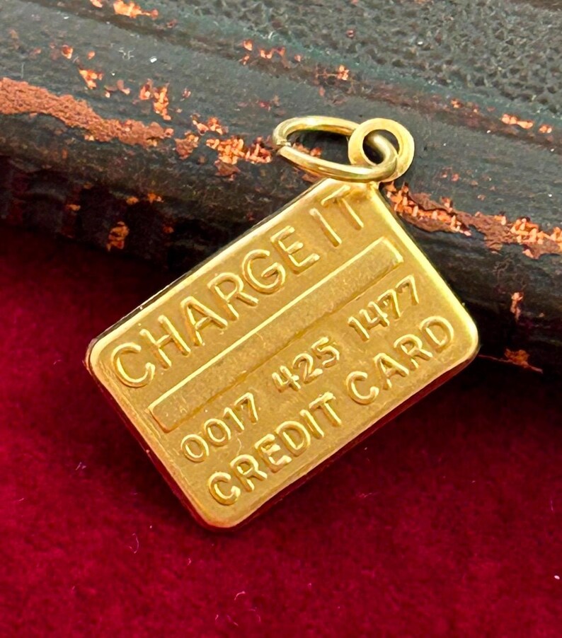 May include: Gold-coloured charm shaped like a credit card with the words "CHARGE IT" and "CREDIT CARD" and the number "0017 425 1477" on it.