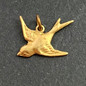 May include: A gold-colored metal charm in the shape of a flying swallow.