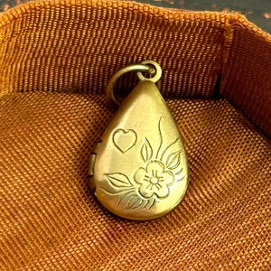 May include: A gold-toned teardrop-shaped locket with a floral design and a small heart engraved on the front.