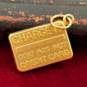May include: A gold-coloured charm shaped like a credit card with the words "CHARGE IT" and "CREDIT CARD" and the numbers "0017 425 1477".