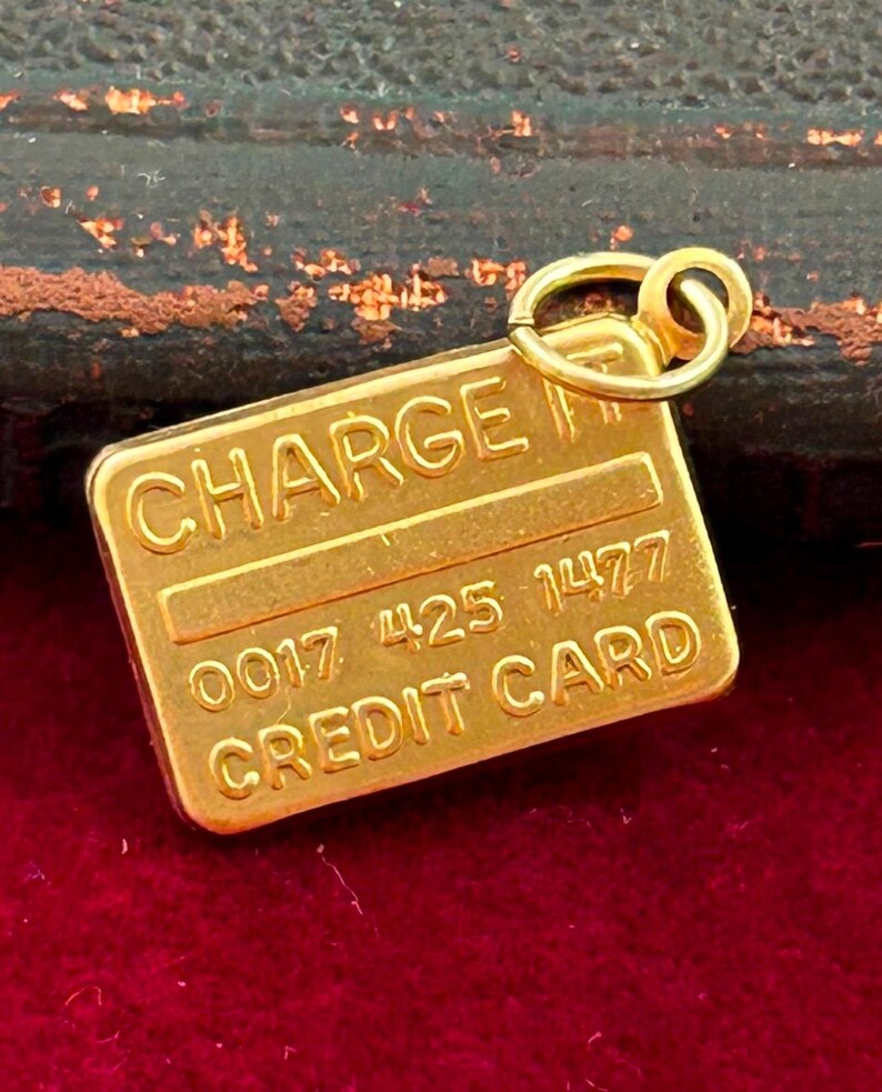 May include: A gold-coloured charm shaped like a credit card with the words "CHARGE IT" and "CREDIT CARD" and the numbers "0017 425 1477".