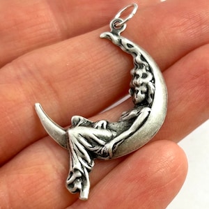 May include: A silver charm pendant featuring a woman sitting on a crescent moon. The charm is detailed and has a vintage style.