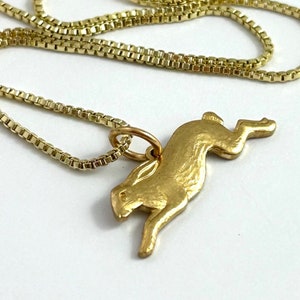 May include: A gold chain necklace with a gold pendant shaped like a leaping hare.