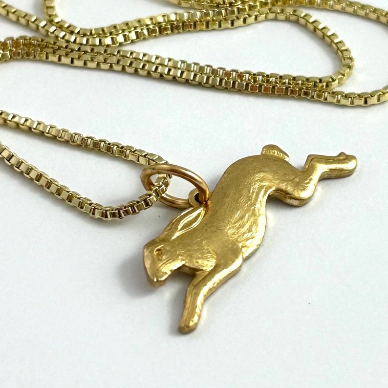 May include: A gold chain necklace with a gold pendant shaped like a leaping hare.