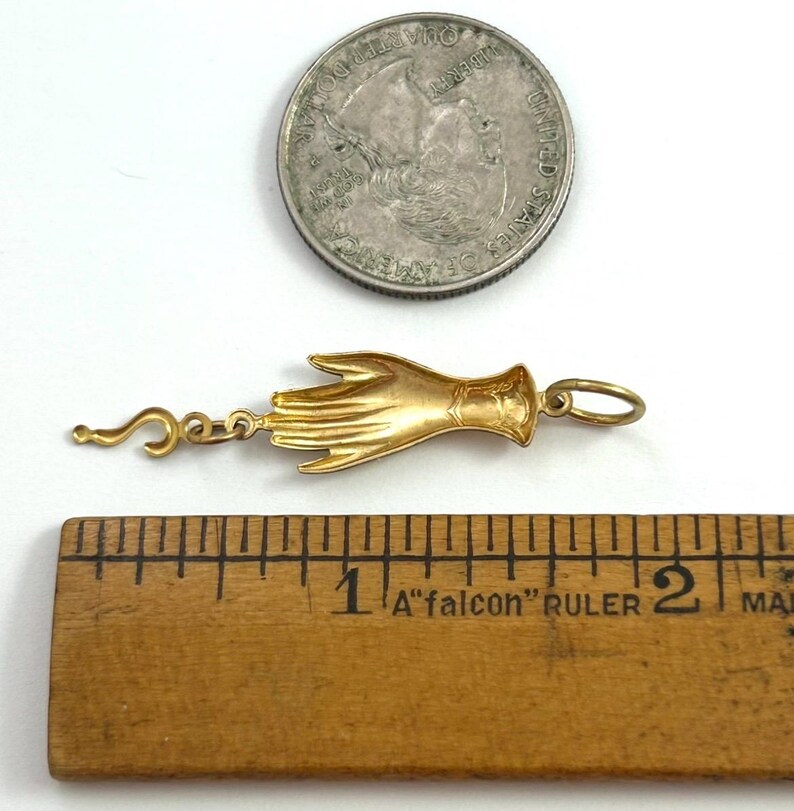 K&ouml;nnte beinhalten: Goldener Anh&auml;nger in Form einer Hand mit einem kleinen Fragezeichen-Anh&auml;nger. Der Anh&auml;nger ist etwa 2,5 cm lang.