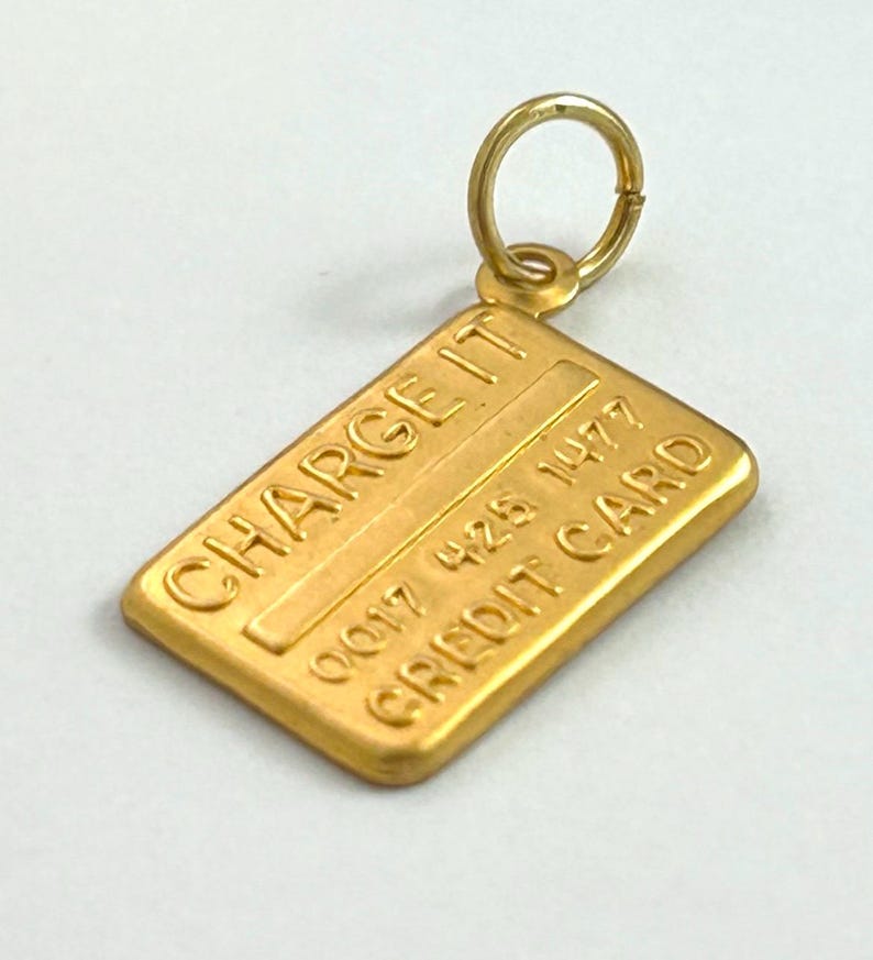 May include: Gold-coloured charm shaped like a credit card with the text "CHARGE IT" and "CREDIT CARD" and the number "0017 428 1477".