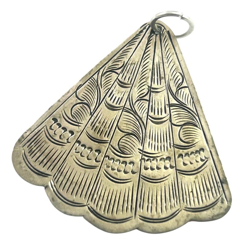 Puede incluir: Colgante plateado en forma de abanico con intrincados patrones grabados. El colgante presenta un borde festoneado y un peque&ntilde;o anillo en la parte superior para sujetarlo. El dise&ntilde;o incluye l&iacute;neas verticales y detalles en espiral, creando una est&eacute;tica vintage.