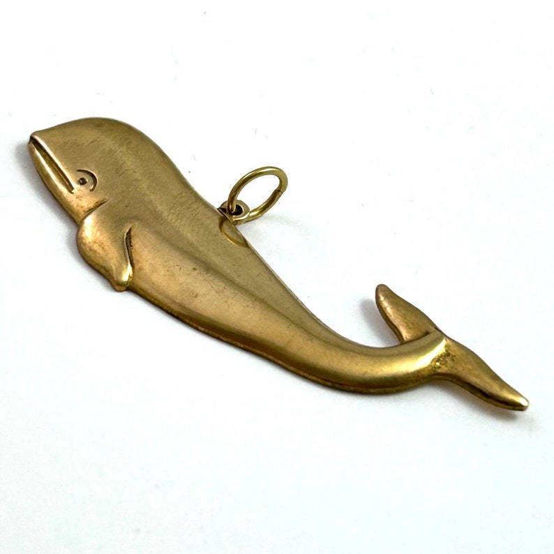 May include: A gold-coloured whale charm with a loop for attaching to a necklace or bracelet.