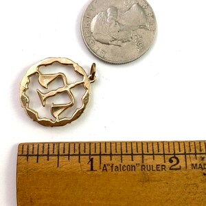 May include: Gold-toned pendant charm featuring a stylized Hebrew letter 'Shin' in a circular frame. The charm is approximately 1 inch in diameter.
