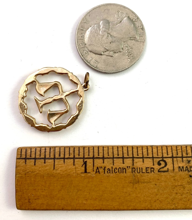 May include: Gold-toned pendant charm featuring a stylized Hebrew letter 'Shin' in a circular frame. The charm is approximately 1 inch in diameter.