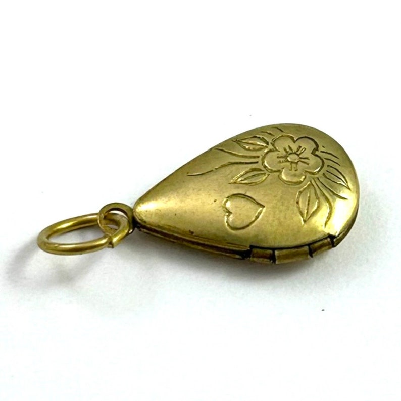 May include: A gold teardrop-shaped locket with a floral design and two hearts. The locket has a hinged opening and a small loop for attaching a chain.
